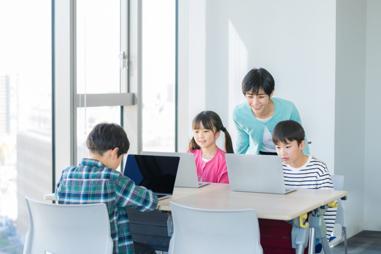 Children learning with laptops and teacher assisting.